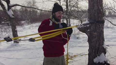 Caucasian man sets slackline between trees in the winter forest. 스톡 동영상 146970288