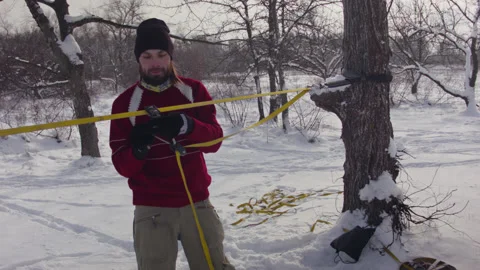 Caucasian man sets slackline between trees in the winter forest. 스톡 동영상 146970854