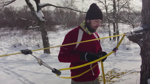 Caucasian man sets slackline between trees in the winter forest. 스톡 동영상 146974852