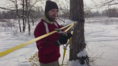Caucasian man sets slackline between trees in the winter forest. 스톡 동영상 146975094