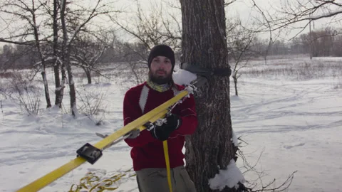Caucasian man sets slackline between trees in the winter forest. 스톡 동영상 146975282