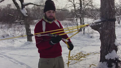 Caucasian man sets slackline between trees in the winter forest. 스톡 동영상 146975467