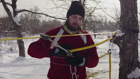 Caucasian man sets slackline between trees in the winter forest. 스톡 동영상 147147493