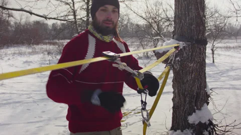 Caucasian man sets slackline between trees in the winter forest. 스톡 동영상 147148746