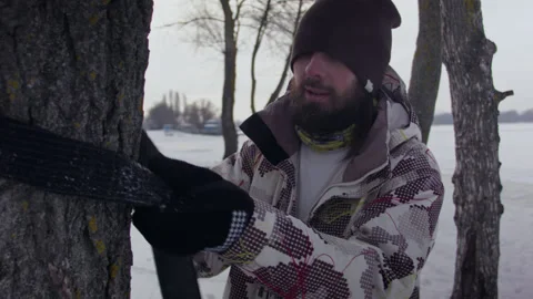 Caucasian man sets slackline between trees in the winter forest. 스톡 동영상 148085119