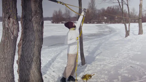 Caucasian man sets slackline between trees in the winter forest. 스톡 동영상 148115306