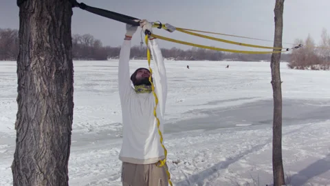 Caucasian man sets slackline between trees in the winter forest. 스톡 동영상 148115577