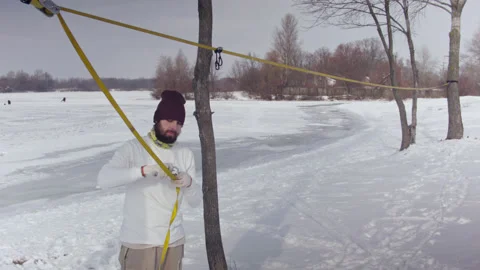 Caucasian man sets slackline between trees in the winter forest. 스톡 동영상 148115633