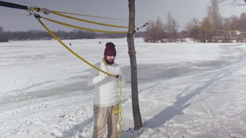 Caucasian man sets slackline between trees in the winter forest. Stock Footage 148164763