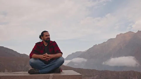 A Caucasian man sits on the edge of a cliff enjoying the mountain landscape Stock Footage 313014190