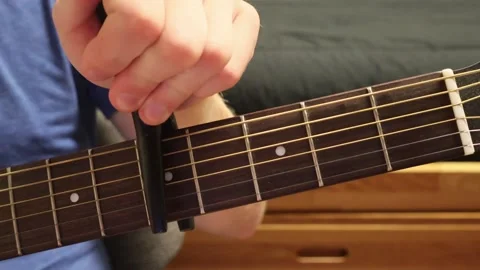 Caucasian man sitting down putting a capo on a guitar Stock Footage 279909217