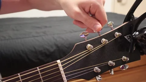 Caucasian man sitting down tuning the A string on a guitar Stock Footage 279909208