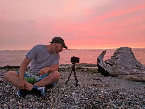 Caucasian Man Smiling While Taking a Photo of Sunset on Beach Stock Photos