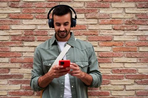 Caucasian man smiling while using phone to send online messages and listen music Stock Photos