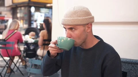 Caucasian man spends time in a cafe, sitting on the terrace, drinking a cup of Stock Footage 139103428