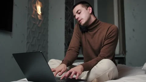 Caucasian man talking on the phone while working with a laptop on bed at home Stock Footage 144311716