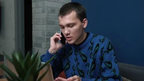 Caucasian man talking on the phone while working with a laptop at home office Stock Footage 144629768