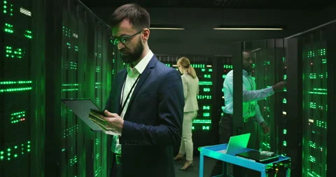 Caucasian man technician in database room with servers, tapping on tablet device Stock Footage 137547373