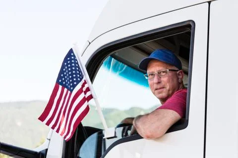 Caucasian man truck driver in the cab of his truck with an American Flag Stock Photos