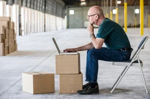 Caucasian man using boxes as desk and working on lap top computer in front of Stock Photos