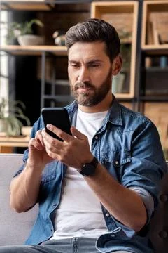 Caucasian man using mobile phone application sitting on sofa at home office Stock Photos