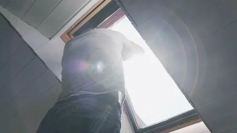 Caucasian man washes the attic window Bright sun illuminates the man in the Stock Footage 153447646