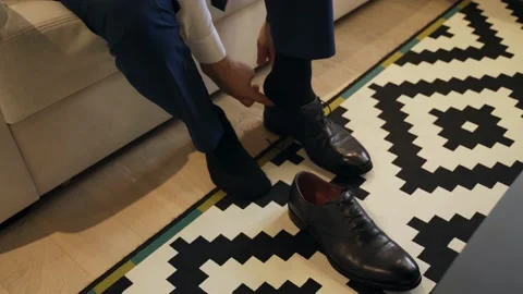 Caucasian man wears dark-colored shoes. The sofa, carpet and table are visible Stock Footage 147313692