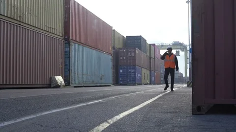 Caucasian man in white hardhat talking by cellphone walking through dockyard Stock Footage 101232600