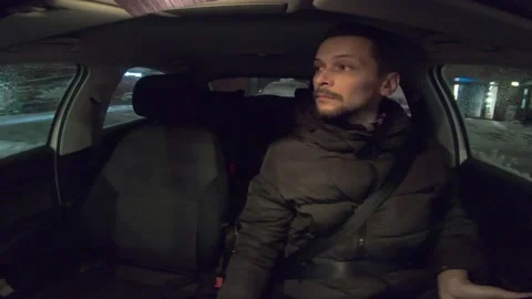 A Caucasian man in a winter jacket rides through the night city driving Stock Footage 237112667