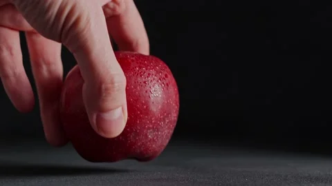 A Caucasian Man's Hand puts a red Apple on the table against a black background Stock Footage 235196175