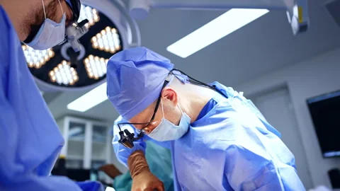Caucasian neurosurgeons co-work at operation. Doctor in surgical loupes uses Stock Footage 331081467