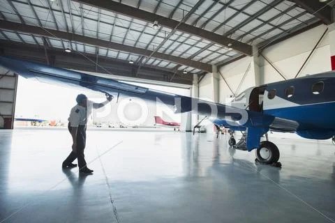 Caucasian Pilot Examining Airplane In Hangar