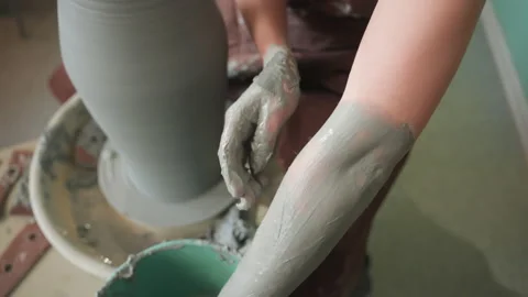 Caucasian potter pulling clay walls with fullarm motion on wheel, arms coated in Stock Footage 346228966