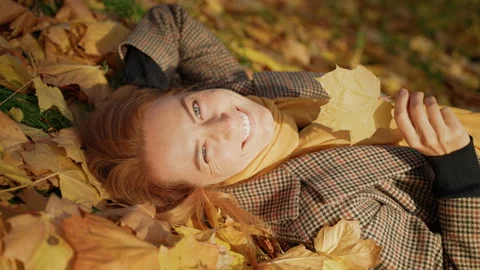 Caucasian red head middle aged woman lies on foliage, enjoys in autumn park Video stock 164143381