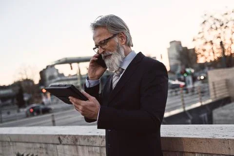 Caucasian senior CEO using a smartphone and smart tablet Stock Photos