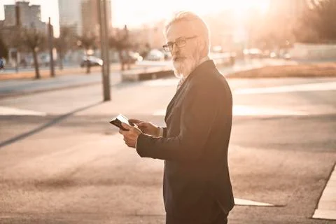 Caucasian senior CEO using a smartphone and smart tablet and looking in the Stock Photos