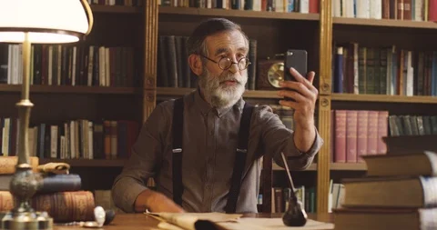 Caucasian senior man with a gray beard and in glasses having a videochat on the Stock Footage