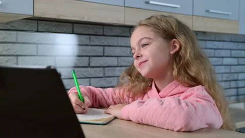 Caucasian small girl is smiling while having online classes on a tablet and 스톡 동영상 150087005