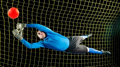 Caucasian soccer goalie jumping in mid-air catching ball at night Stock Photos