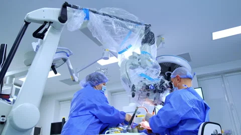 Caucasian surgeon sits at microscope performing operation. Female medic assists Stock Footage 333337088