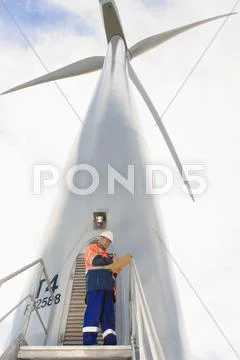 Caucasian Technician Reading Paperwork Under Wind Turbine