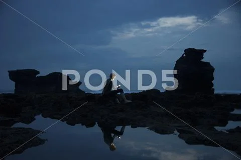 Caucasian teenage boy exploring rocky tidal pools at night, Canggu, Bali, Stock Photos