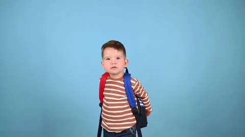 Caucasian toddler boy with a backpack on a blue background. Little schooler Stock Footage 214343586