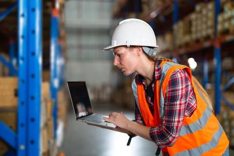 Caucasian warehouse worker checking the package using a laptop in the large dist Foto stock