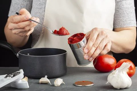A caucasian woman is adding tomato paste from a can into a dish she is prepar Stock Photos