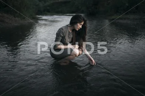 Caucasian woman crouching in remote stream Stock Photos