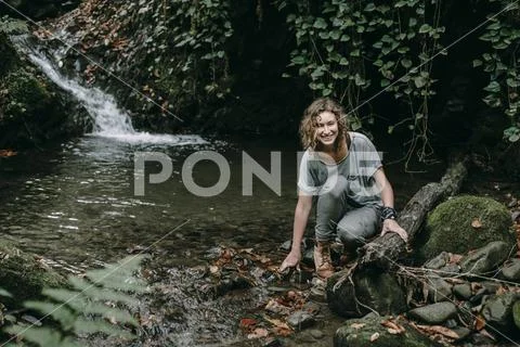 Caucasian woman crouching on rock in forest stream Stock Photos