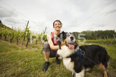 Caucasian Woman Petting Dog In Vineyard