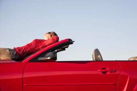 A Caucasian woman  resting on the hood of her convertible sports car at a rest Stock Photos