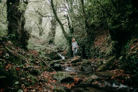 Caucasian woman standing on rock near forest stream Stock Photos